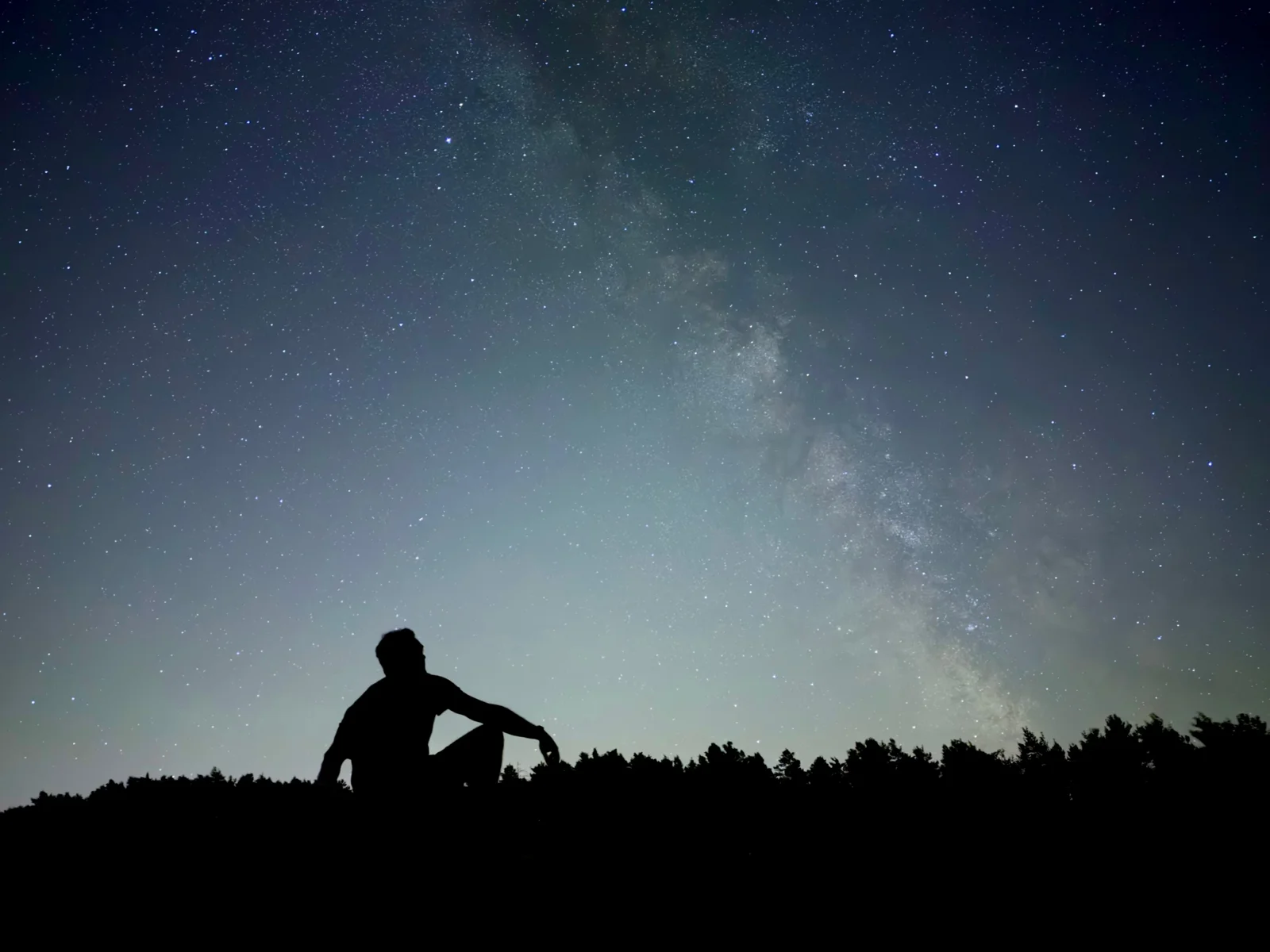 Pessoa em silhueta sob um céu estrelado, fotografada com modo Noite